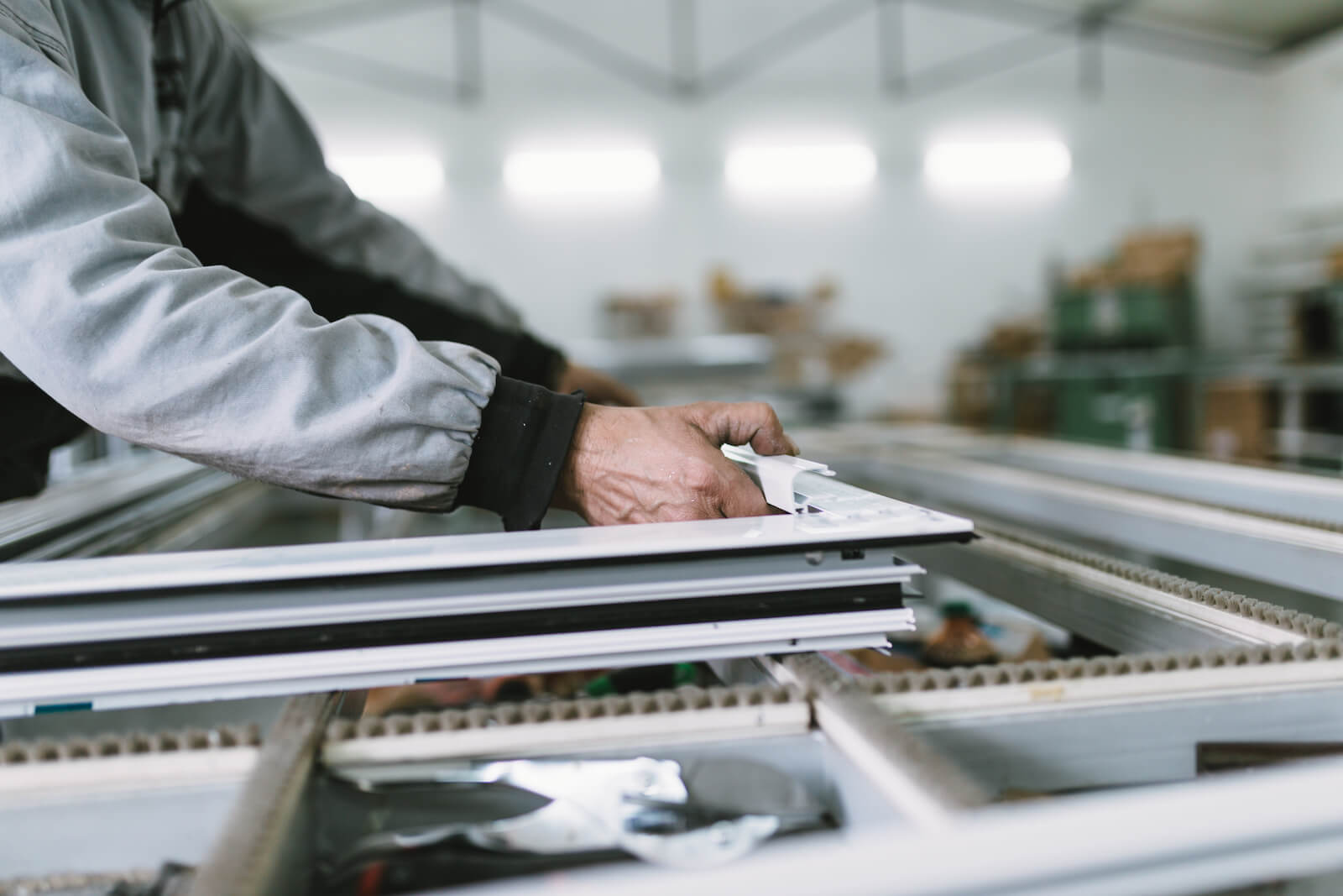 A close-up of a worker assembling an aluminium window frame in a factory setting, highlighting the precision required in the fenestration industry.